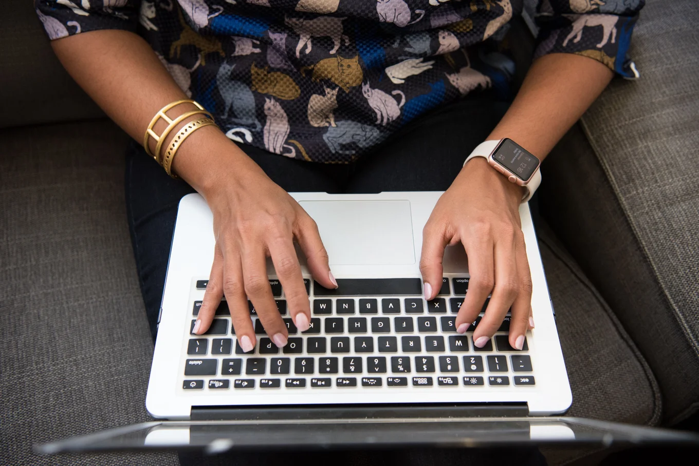 Hands typing on a laptop keyboard, watch visible.
